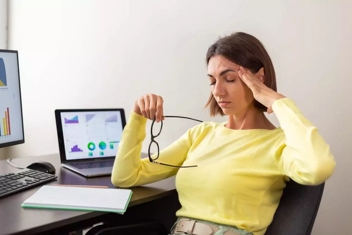 Stressed businesswoman analyzing financial charts on her computer, holding glasses, and massaging her temple.
