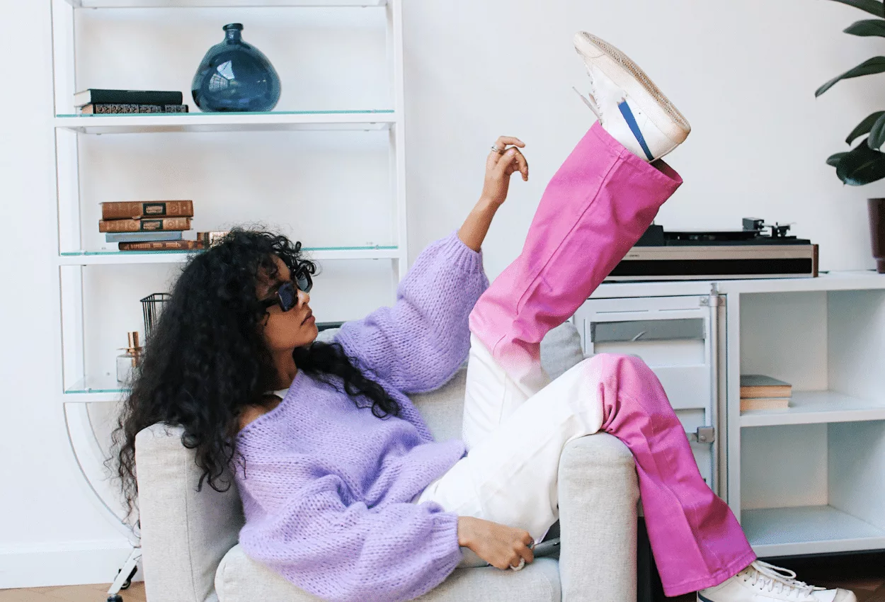 Fashionable woman in purple sweater and pink pants lounging on a chair