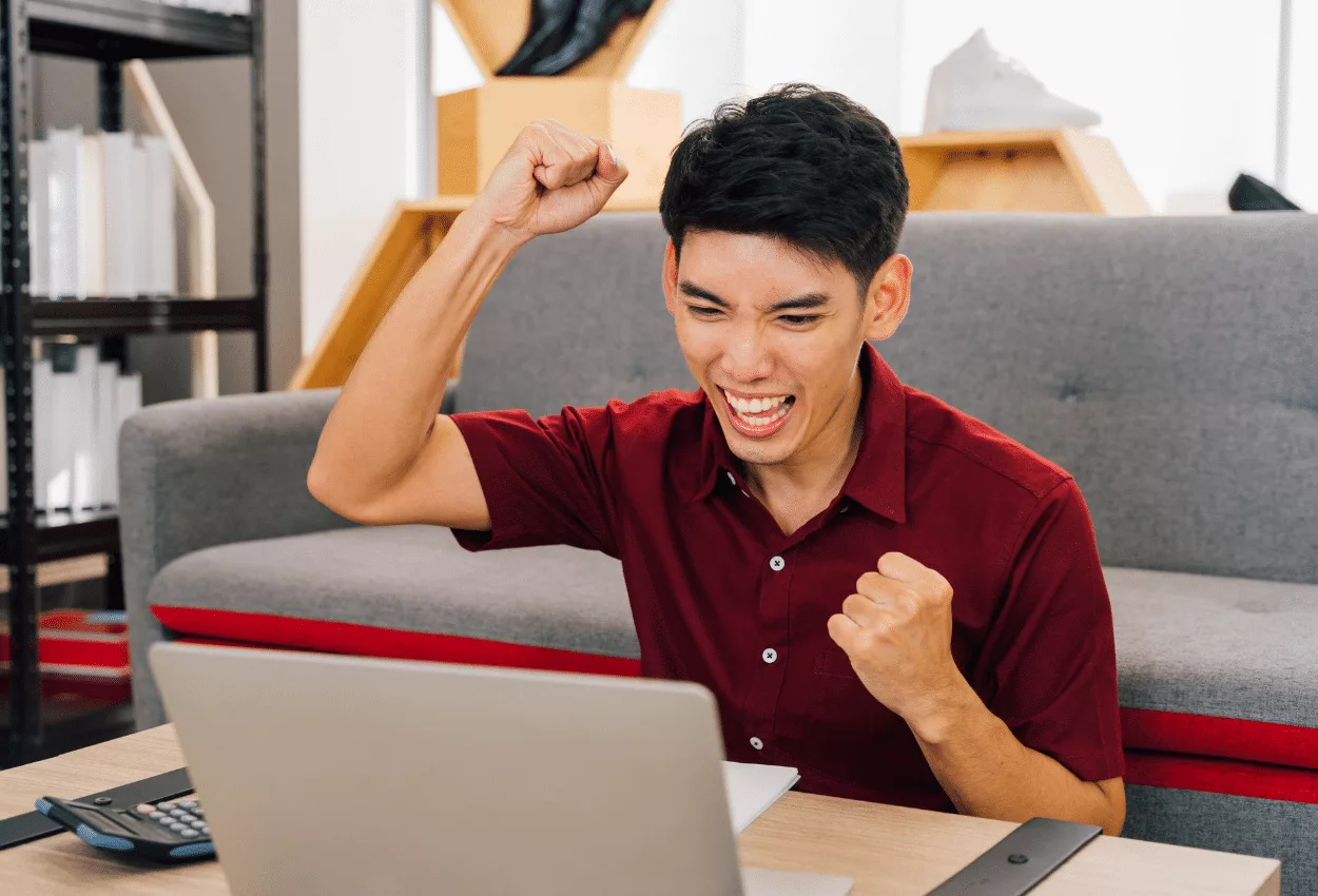 Excited young man celebrating success while looking at his laptop