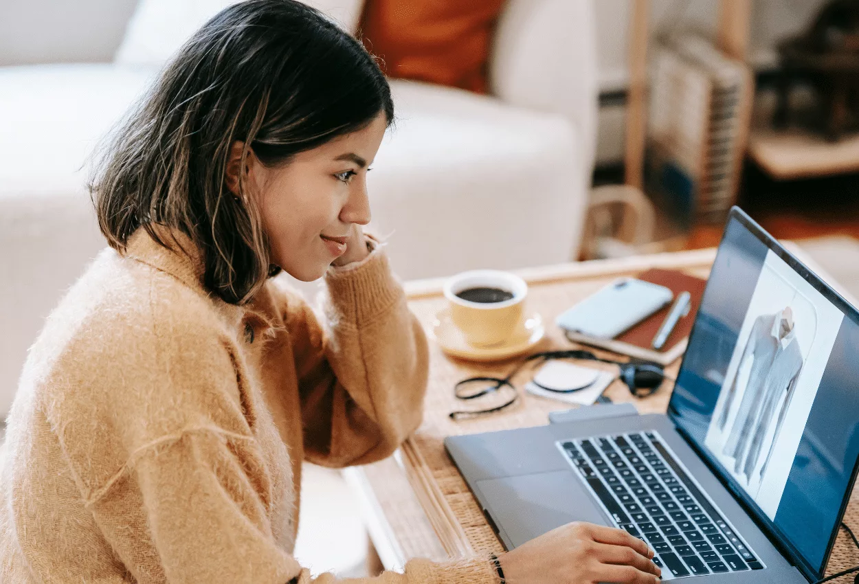 Woman browsing clothes online while enjoying coffee at home.