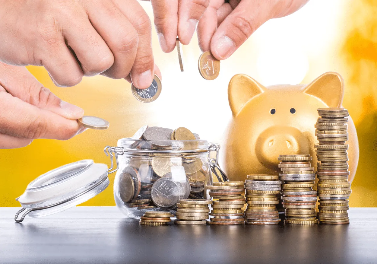 Hands putting coins in a jar and a golden piggy bank surrounded by stacks of coins