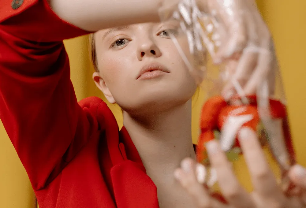 Woman in a red blazer with a serious expression holding a transparent bag with red flowers against a yellow background.