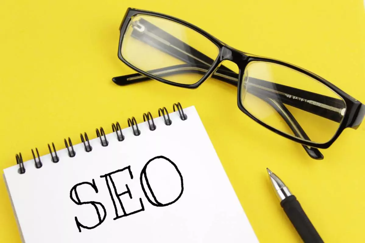 SEO concept with blank paper, pen, and glasses on a yellow background.